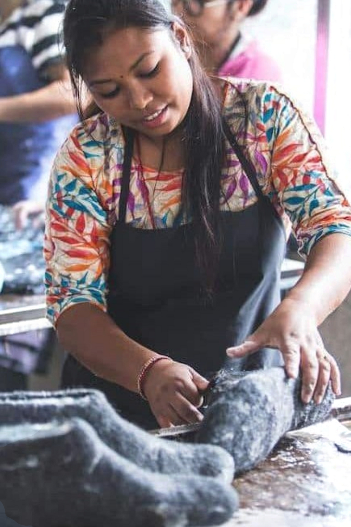 SHUS.dk håndværker i Nepal der omhyggeligt arbejder med en grøn uldtøffel af 100% ren uld og skridsikker gummisål